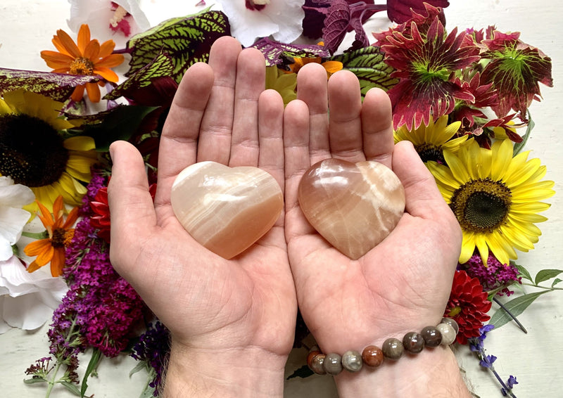 two hands holding an orange with white swirls blood orange calcite crystal heart.
