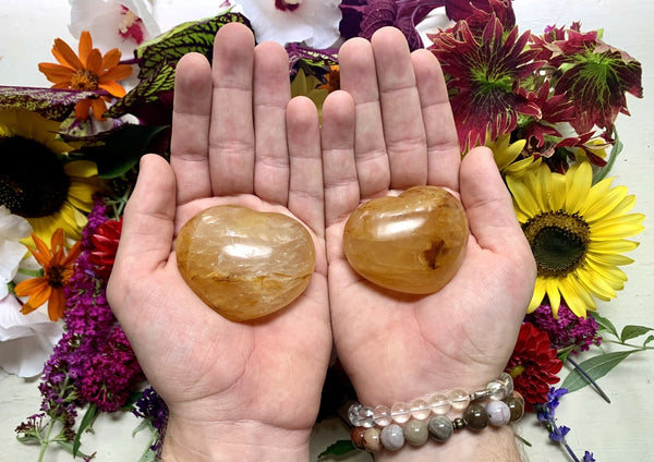 two palms holding a yellow toned golden healer crystal heart with quartz.