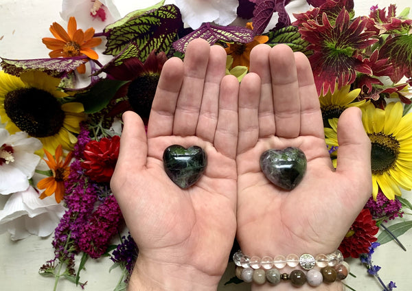 two male hands holding two rainbow fluorite crystal hearts 