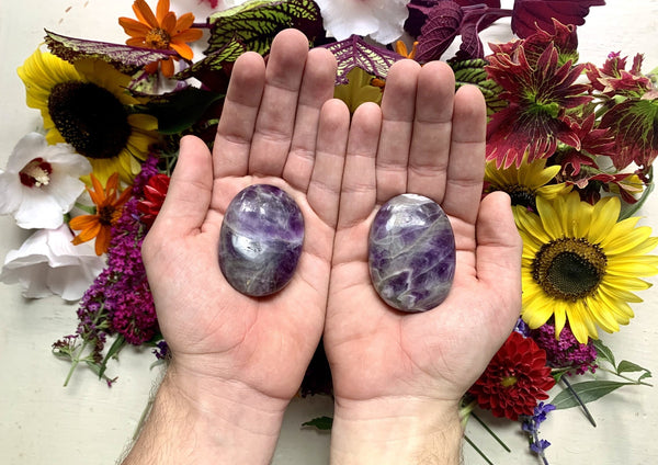 two flat purple and grey and white amethyst palm stones in the palm of male hands.