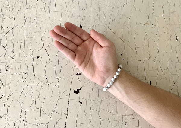 one white howelite energy bracelet on the wrist of a male on a white tabletop