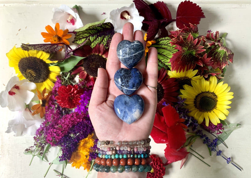 one hand holding three small blue sodalite hearts with black and white veins. 