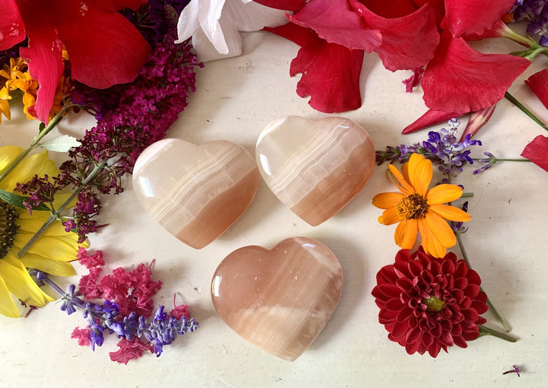 three orange with white swirls blood orange calcite crystal hearts on tabletop with flowers.