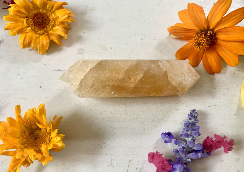 one light yellow citrine double terminated point on tabletop with yellow flowers.