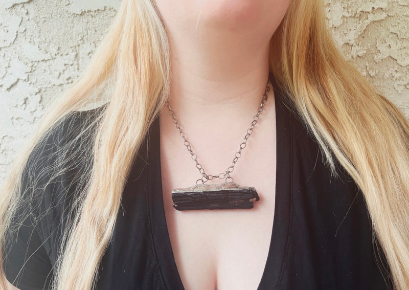 large black tourmaline hanging on silver link chain on model's neck.