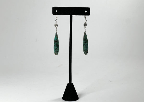 African turquoise earrings with silver swoosh detail hanging on black t stand. 