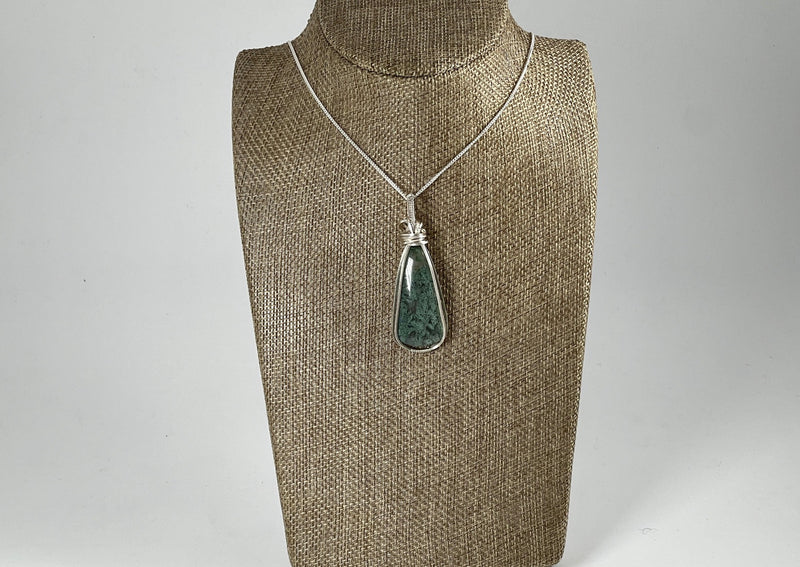 Tear drop shaped Moss Agate pendant wrapped in silver on silver chain hanging on linen bust display