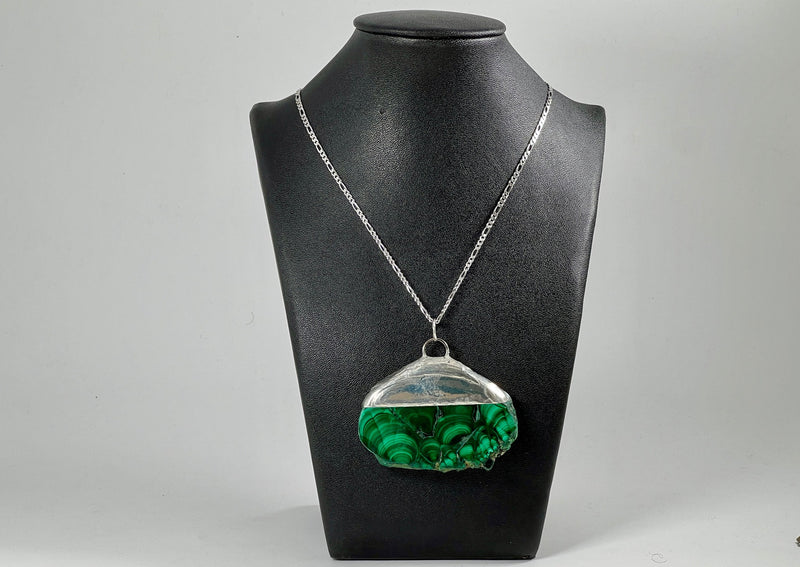 Large Malachite slab soldered and hanging on sterling silver chain around black leather bust display. 