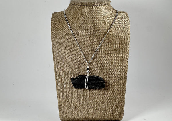 large raw black tourmaline hanging on silver chain displayed on linen bust. 