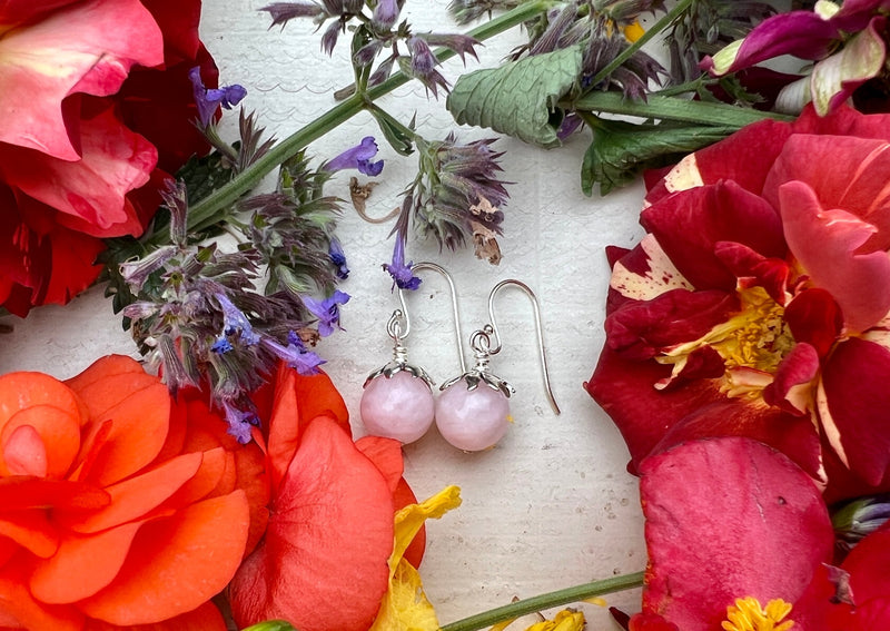 rose quartz earrings on a table with flowers. 