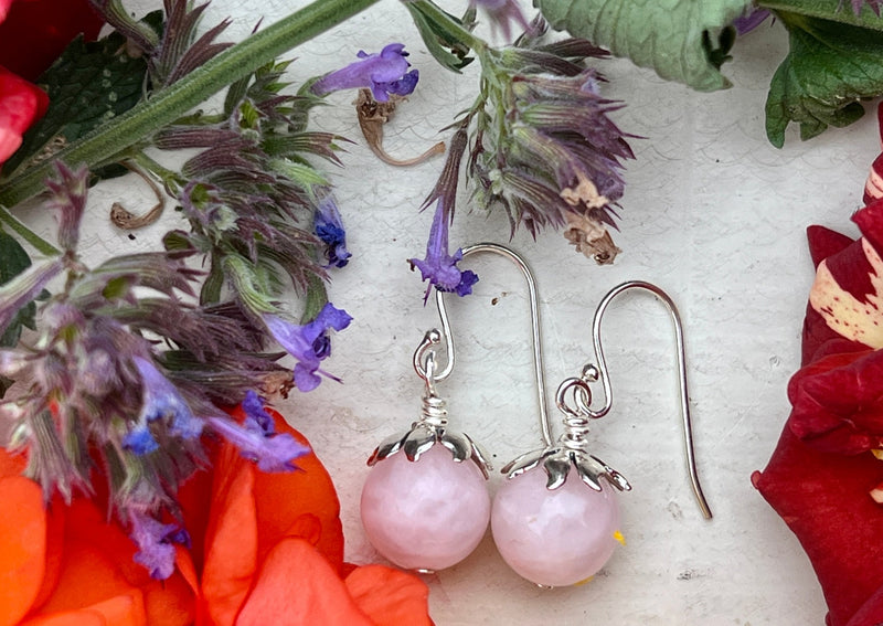 rose quartz earrings on a table with flowers. 