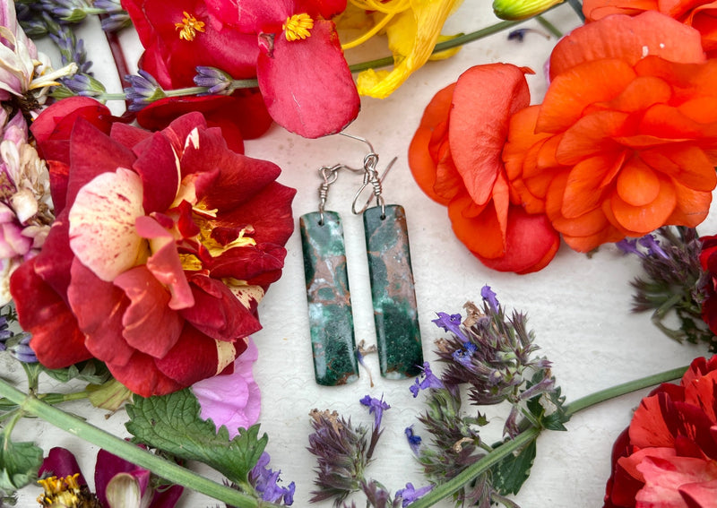 Malachite and Chrysocolla earrings on table with flowers. 