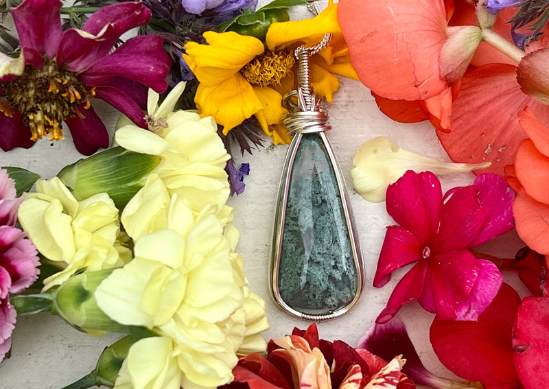 Moss Agate pendant on table with flowers. 