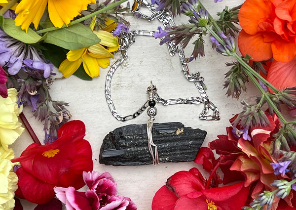 Black  Tourmaline pendant on table with flowers.