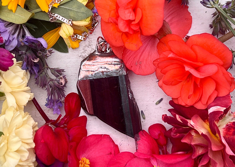 Red tigers eye pendant on table with flowers.